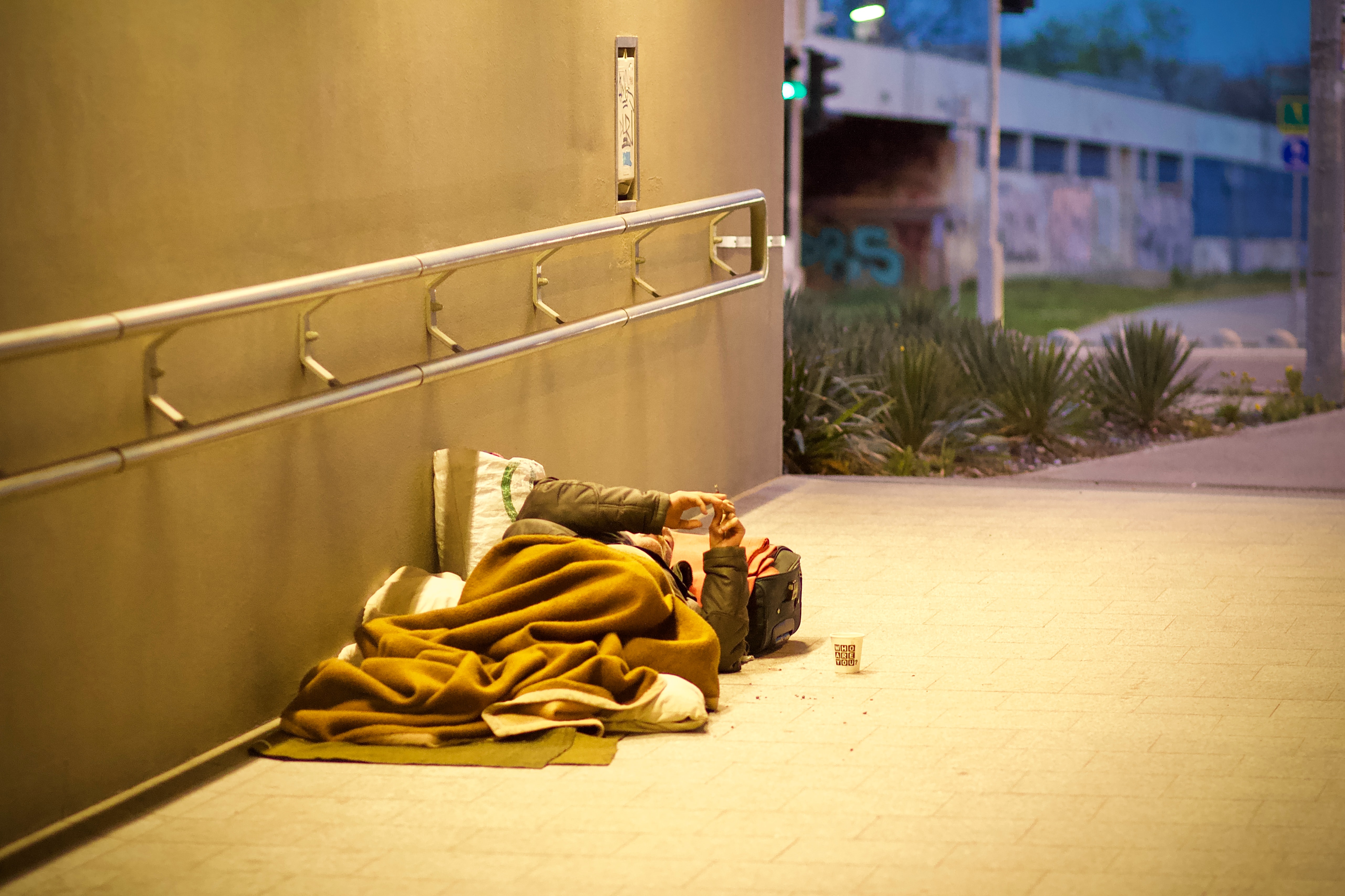 An image of a homeless person laying down inside a tunnel with a blanket.